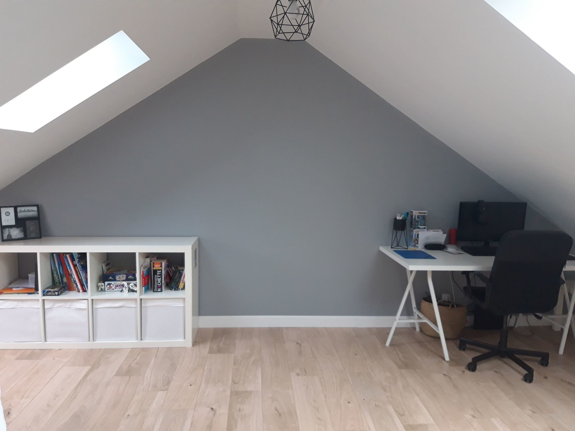 Pièce sous les combles rénovée avec un mur gris, un parquet en chêne clair, une étagère blanche et un bureau avec chaise noire.