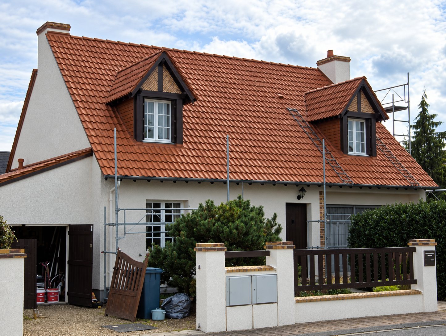 Maison blanche à deux lucarnes dont le toit en tuiles brunes vient d'être rénové, avec un échafaudage encore visible sur le côté.