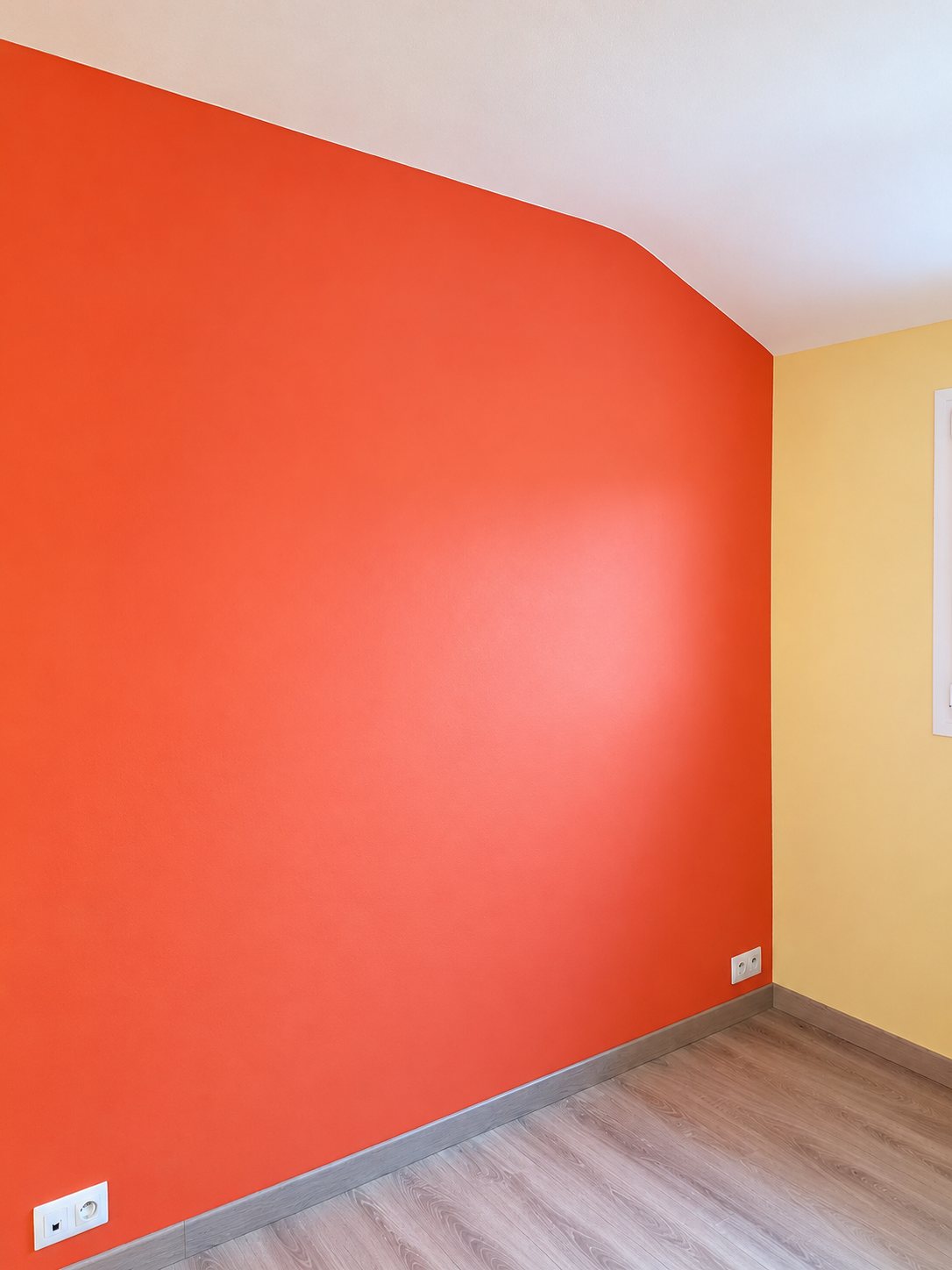 Pièce rénovée avec un mur d'accent orange, des murs beige clair, des plinthes grises et un parquet clair.