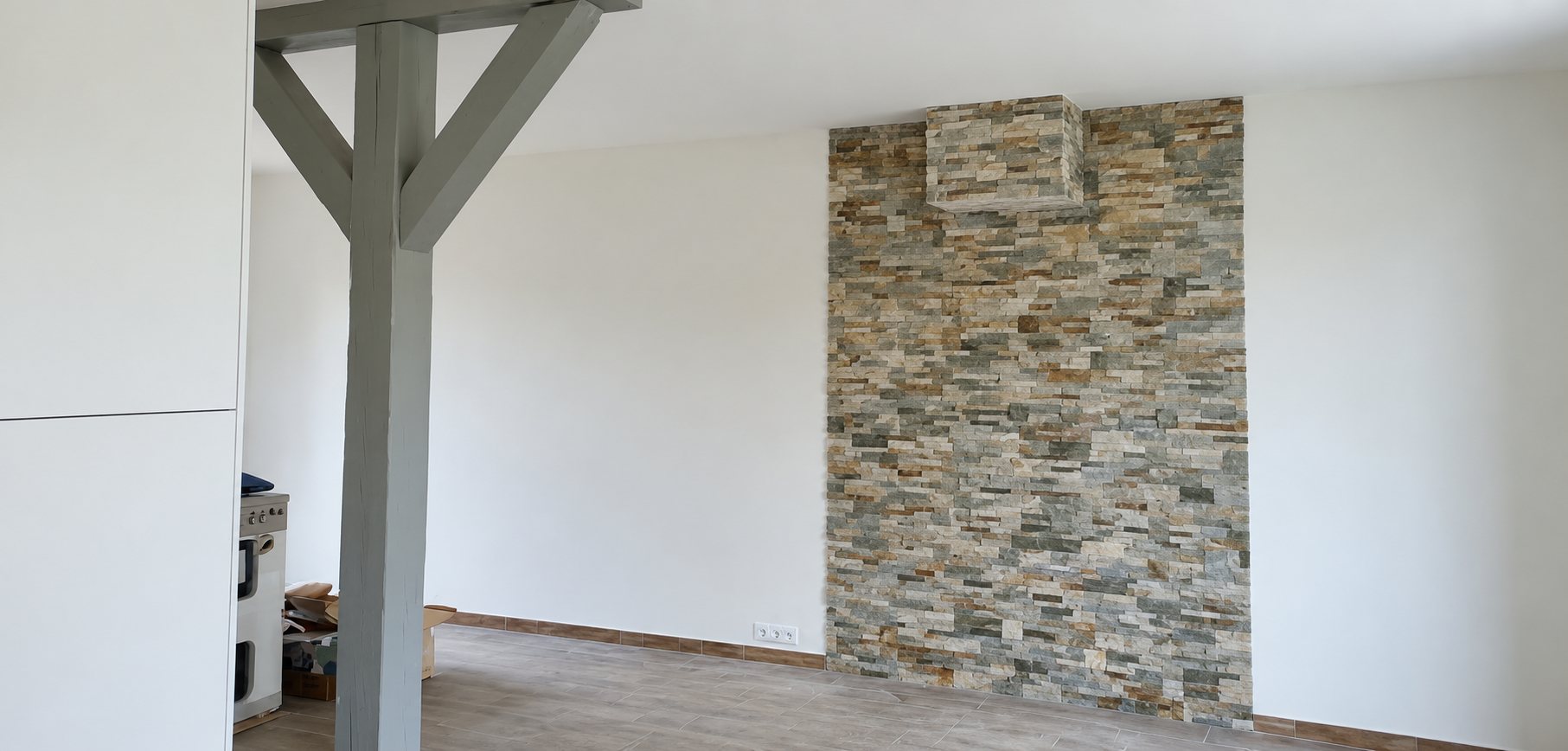 Pièce rénovée aux murs blancs avec un pan de mur en pierre de parement et un poteau en bois peint en gris.