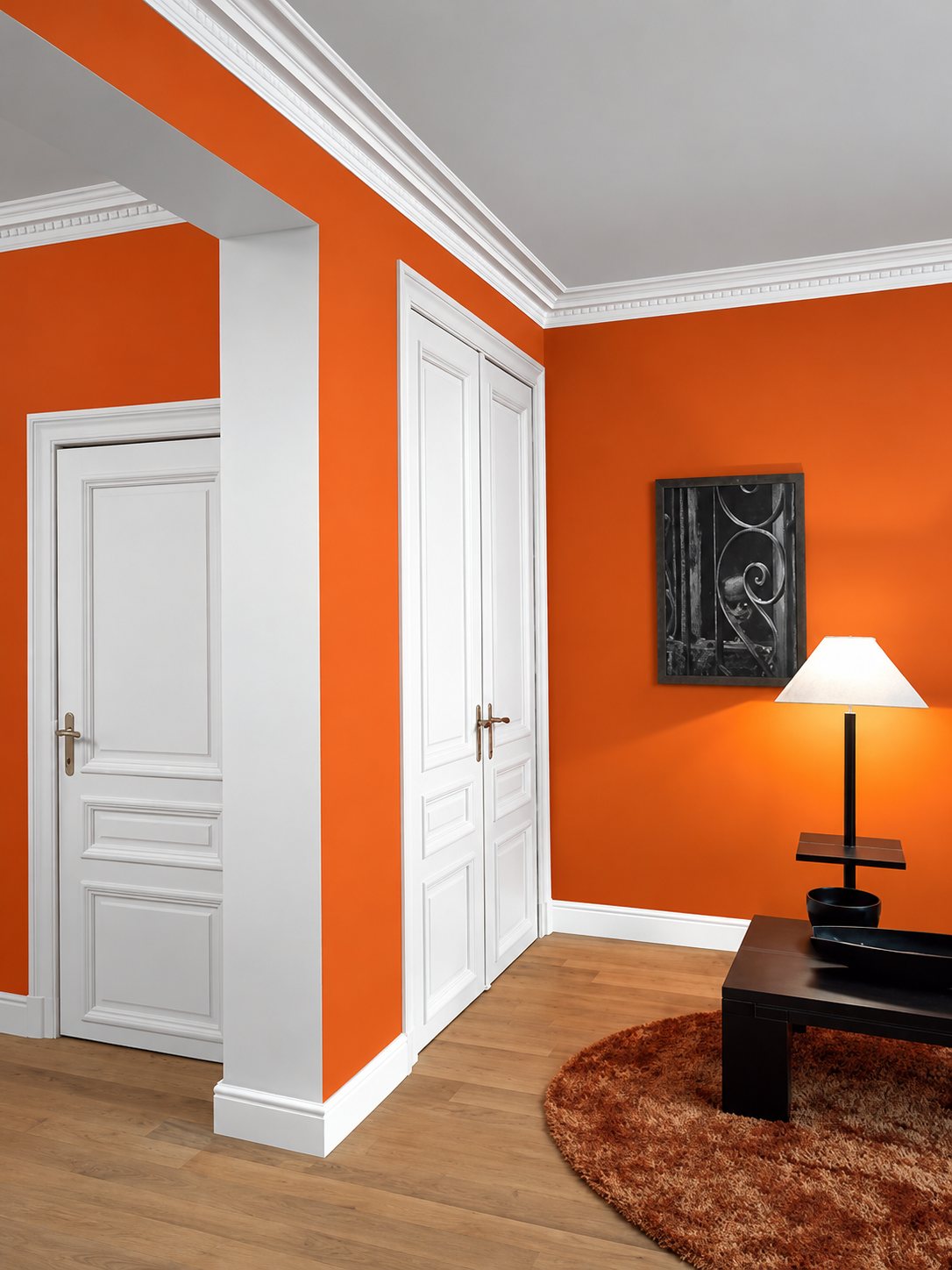 Intérieur aux murs orange vif avec des portes blanches à panneaux, une corniche blanche, une lampe allumée et une table basse sur un tapis marron.